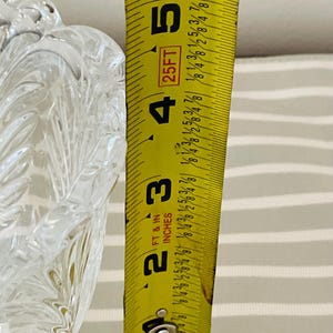 Peut inclure: Un bol en verre clair et d&eacute;coratif avec un motif textur&eacute; en forme de feuille. Un ruban &agrave; mesurer jaune indique que la hauteur du bol est d'environ 10 cm. Le ruban est gradu&eacute; en pieds et en pouces.