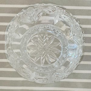 Peut inclure: Bol en verre transparent avec des motifs complexes de feuilles et de fleurs. Le bol pr&eacute;sente un motif en &eacute;toile au centre et est pos&eacute; sur un fond ray&eacute;. Le bol est probablement utilis&eacute; pour servir ou exposer.