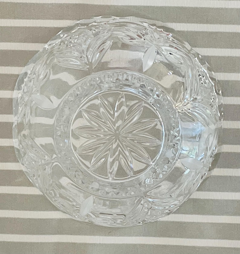 Peut inclure: Bol en verre transparent avec des motifs complexes de feuilles et de fleurs. Le bol pr&eacute;sente un motif en &eacute;toile au centre et est pos&eacute; sur un fond ray&eacute;. Le bol est probablement utilis&eacute; pour servir ou exposer.