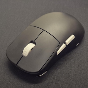 May include: A matte black computer mouse featuring a smooth, rounded shell, two primary click buttons, a white textured scroll wheel positioned in the center, and two white side buttons located on the left edge of the device's ergonomic frame.