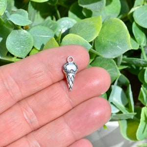 May include: Silver charm in the shape of an ice cream cone. The charm is detailed with a waffle cone texture and a rounded top.