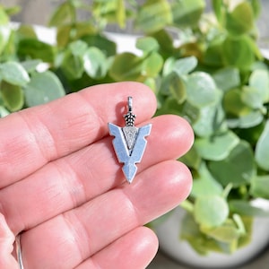 May include: Silver arrowhead pendant charm with a detailed design. The pendant is small and has a pointed tip.