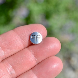 May include: A silver charm with the astrological symbol for Aries, a ram's horns.