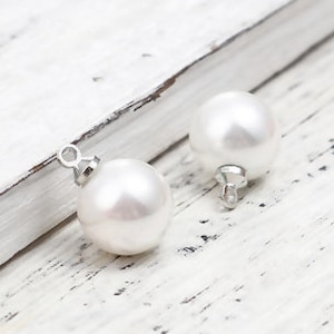 May include: Two white pearl-like beads with silver loops for hanging. The beads are round and smooth.