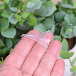 May include: A clear plastic funnel with a narrow spout, held in a hand.