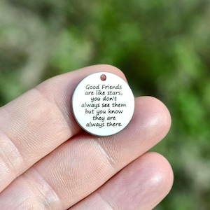 May include: A small, circular, silver-toned charm with a hole at the top. The charm features the text "Good Friends are like stars, you don't always see them but you know they are always there." in black.