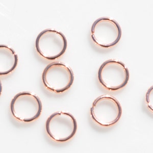 May include: A group of ten rose gold jump rings, which are small metal rings used for connecting jewelry components.