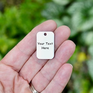 May include: A white metal tag with rounded corners and a hole at the top. The tag has the text "Your Text Here" printed on it.