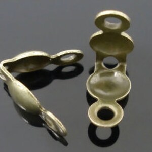May include: Two antique gold metal corner connectors with rounded edges and two small holes. The connectors are designed to join two pieces of fabric or leather together.