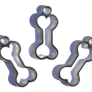 K&ouml;nnte beinhalten: Drei silberne Metall-Anh&auml;nger in Form von Hunde-Knochen. Jeder Anh&auml;nger hat oben eine Schlaufe zum Anbringen an eine Halskette oder ein Armband.