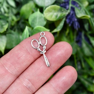 May include: Silver-toned metal charm shaped like a pair of scissors with a decorative floral design.