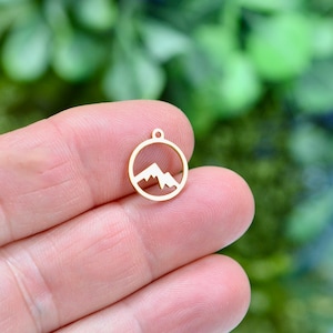 May include: Gold-colored metal charm with a mountain silhouette inside a circle.