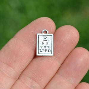 May include: Silver charm with an eye chart on it. The chart reads "E, FP, TOZ, LPED".