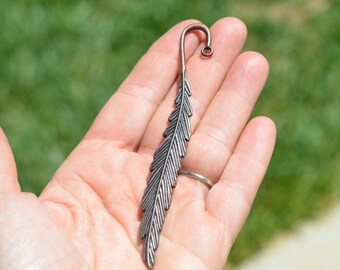 May include: A silver metal bookmark shaped like a feather with a loop at the top.