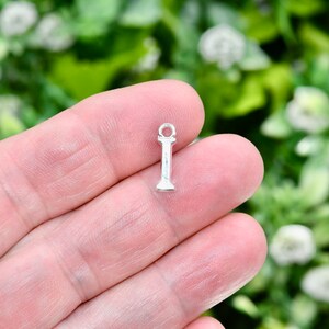 May include: Silver charm in the shape of the letter I. The charm has a loop at the top for attaching to a bracelet or necklace.