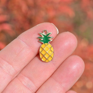 May include: A gold-colored pineapple charm with a yellow body and green leaves. The charm is small and would be perfect for adding to jewelry or crafts.
