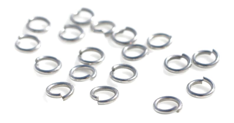 May include: A close-up of a pile of silver jump rings, a type of jewelry finding used for connecting chains, cords, and other jewelry components.
