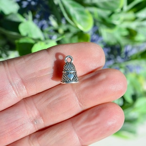 May include: Silver thimble charm featuring a heart design. The charm is small and intricate, ideal for adding a touch of vintage style to jewellery or crafts.