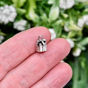 May include: Silver charm in the shape of a wrapped gift box with a bow on top. The charm is small and detailed.