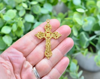 Puede incluir: Un colgante de cruz de metal dorado con intrincados diseños florales. La cruz es ornamentada y tiene una superficie texturizada detallada.