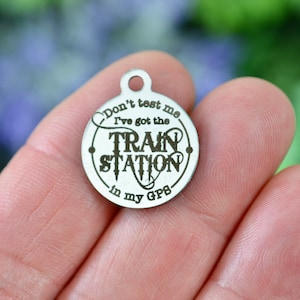 May include: A silver charm with the text "Don't test me I've got the train station in my GPS" engraved on it.