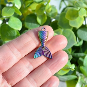 May include: A rainbow iridescent mermaid tail charm with a scaly design. The charm is made of metal and has a hole at the top for attaching to a necklace or bracelet.