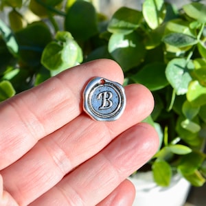 May include: Silver charm with a wax seal design featuring the letter "B" in a vintage font.