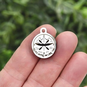 May include: A circular silver-toned metal charm featuring an engraved design of a kayak with paddles, mountain peaks, and wavy lines. The text "RELAX! YOU'RE ON LAKE TIME" is inscribed along the bottom edge, with the number 5 at the top and bottom.
