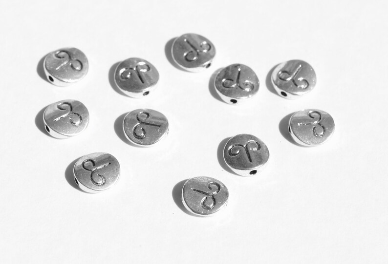 May include: Ten silver-toned metal beads with a raised Aries zodiac symbol on each bead. The beads have a hole through the center for stringing.
