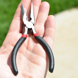 May include: A pair of black and red needle-nose pliers with a silver metal head.