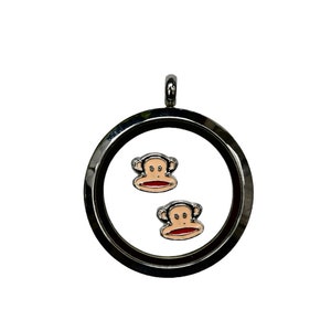 May include: A black metal locket with two small monkey charms inside. The monkeys have brown fur, red lips, and black eyes.