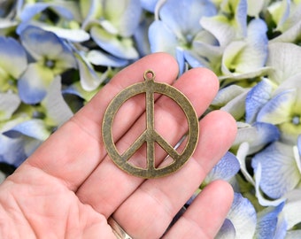 May include: A bronze peace symbol pendant, featuring a circular design with a vertical line and two angled lines. The charm has a small loop at the top for attaching to jewellery or crafts.