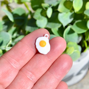 May include: White enamel charm shaped like a fried egg with a yellow yolk.