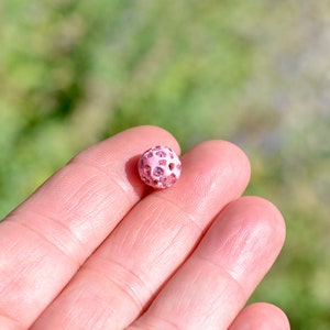 May include: A single pink bead with a textured surface and a glittery finish.