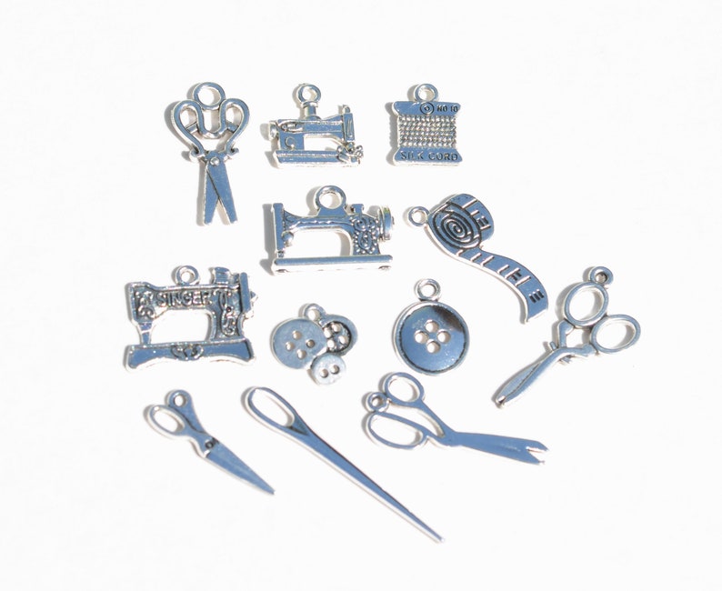 May include: A collection of silver-toned metal charms with sewing themes. The charms include sewing machines, scissors, spools of thread, buttons, and a measuring tape.