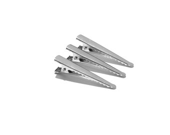 May include: Three silver alligator clips, also known as hair clips, are arranged in a triangular shape on a white background.