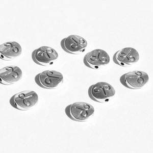 May include: Silver metal beads with a zodiac symbol, Aries, engraved on each bead. The beads are round and have a hole in the center for stringing.