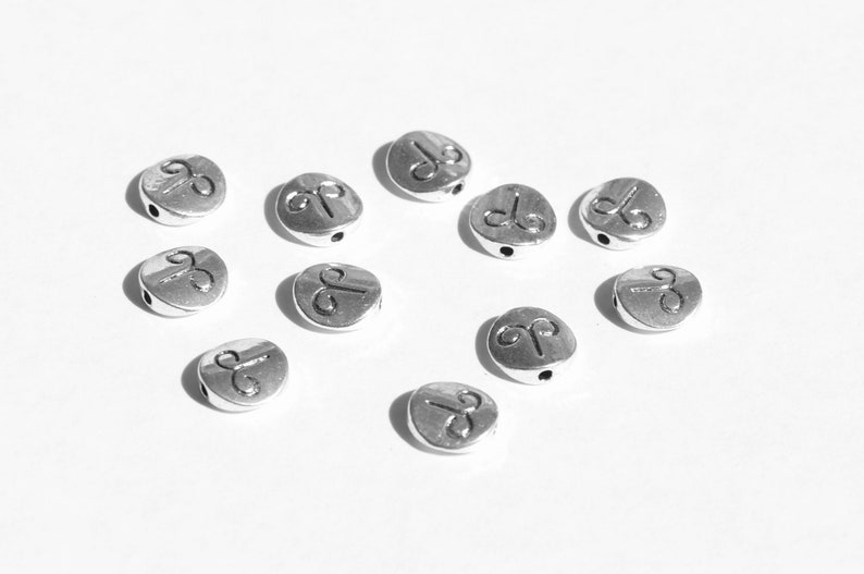 May include: Silver metal beads with a zodiac symbol, Aries, engraved on each bead. The beads are round and have a hole in the center for stringing.
