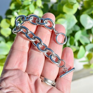 May include: A silver chain bracelet with a toggle clasp. The bracelet is made of thick, chunky links.