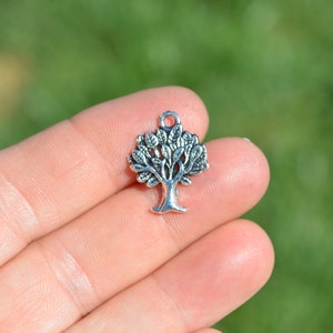 May include: Silver charm in the shape of a tree with detailed branches and leaves.