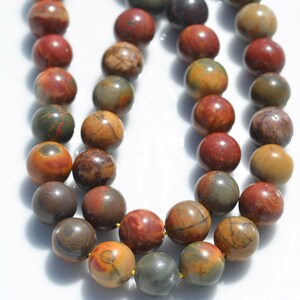 Puede incluir: Una hebra de cuentas redondas de piedras preciosas multicolores. Las cuentas son una mezcla de marr&oacute;n, rojo y amarillo con patrones en espiral. Las cuentas est&aacute;n enhebradas en un hilo dorado.