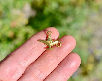 May include: A gold-colored metal genie lamp charm with a loop at the top for attaching to a necklace or bracelet.