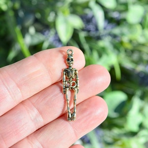 May include: Gold-toned skeleton charm pendant. The skeleton is standing with its arms at its sides.