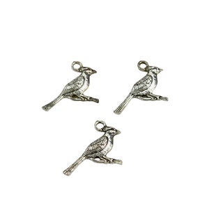 K&ouml;nnte beinhalten: Drei silberne Vogel-Anh&auml;nger aus Metall mit detailliertem Design. Die V&ouml;gel sitzen auf einem Ast mit ausgebreiteten Fl&uuml;geln.