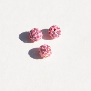 May include: Three pink round beads covered in small pink rhinestones.