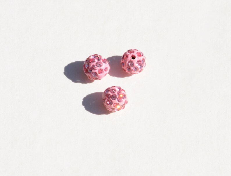 May include: Three pink round beads covered in small pink rhinestones.