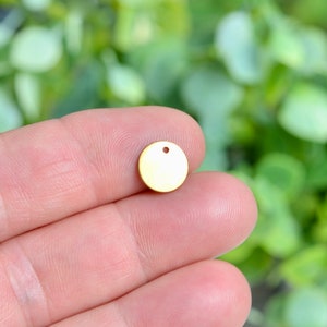 Op de afbeelding: Een gouden metalen cirkel met een klein gaatje in het midden. De cirkel heeft een diameter van ongeveer 2,5 cm.