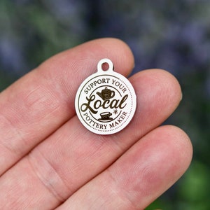 May include: A silver charm with the text "Support Your Local Pottery Maker" and a graphic of a teapot and teacup.