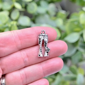May include: Silver charm in the shape of bell bottom pants with a floral design.