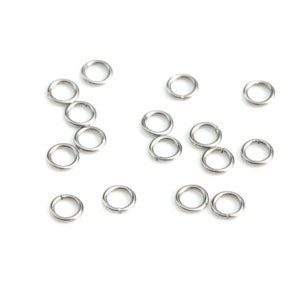 May include: A collection of silver jump rings, scattered on a white background. The rings are small and circular, with a smooth, metallic finish.